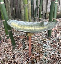 a metal bowl sitting on top of a wooden table in front of bamboo trees and grass