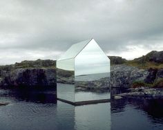 a mirror sitting on top of a body of water next to a rocky shore under a cloudy sky