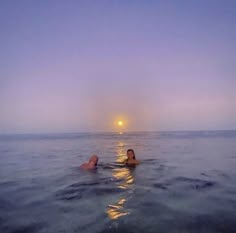 two people are swimming in the ocean at sunset or dawn with their backs turned to the camera