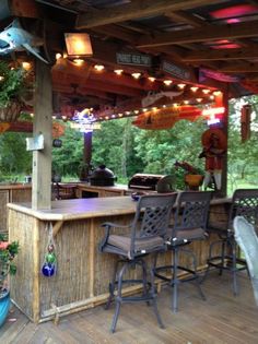 an outdoor bar with chairs and lights hanging from it's roof, on a deck