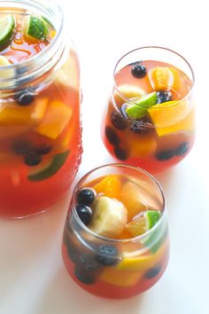 two glasses filled with fruit and ice on top of a white table next to each other