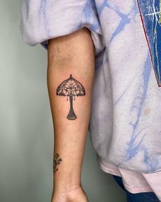 a person with a tattoo on their arm holding onto a small umbrella shaped like a tree