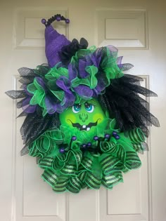 a green and purple wreath with a witch's face on it hanging from the front door