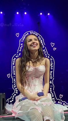 a woman in a corset sitting on a stage with purple lights behind her