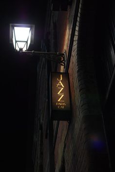 a street sign hanging from the side of a brick building with a light on it