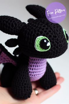 a small crocheted black dragon with green eyes sitting on someone's hand