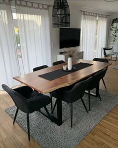 a dining room table with black chairs and a flat screen tv mounted on the wall