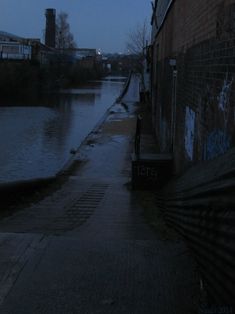 an empty street next to a body of water at night with graffiti on the wall