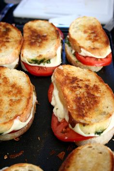 several grilled sandwiches sitting on top of a black pan with tomato slices and cheese