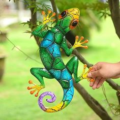 a hand holding a colorful glass lizard hanging from a tree