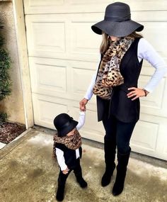 a woman holding the hand of a small child in front of a garage door wearing a hat and scarf