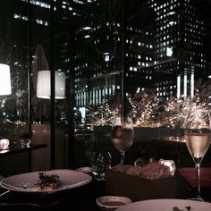 two plates with food and wine on a table in front of a cityscape