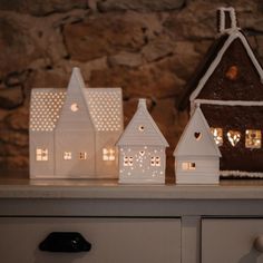 three small white houses sitting on top of a table next to a wall with lights