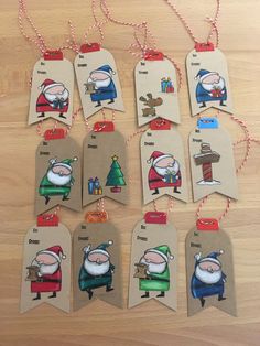 christmas tags with santa claus and other cartoon characters hanging from strings on a wooden table