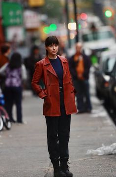 a woman standing on the side of a road wearing a red jacket and black pants