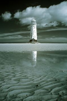 a white lighthouse sitting on top of a sandy beach next to the ocean under a cloudy sky