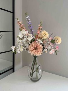 a vase filled with lots of flowers on top of a white table next to a mirror