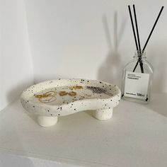 a white ceramic dish with black speckles on it next to an empty bottle