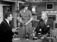 three men and a woman sitting around a table talking to each other in a living room