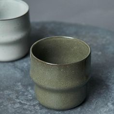 two gray cups sitting on top of a table next to each other, with one empty cup in the middle