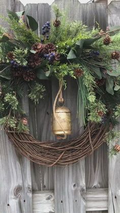 a wreath hanging on the side of a wooden fence with a bell and evergreens