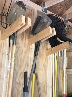 there are many different tools hanging on the wall in this room, including shovels and rakes