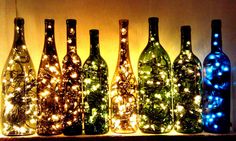 lighted wine bottles are lined up on a shelf in front of a wall with christmas lights