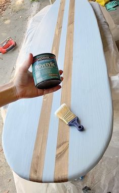 a person holding a can of paint on top of a surfboard that is being painted