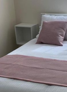 a bed with pink and white pillows on top of it next to a night stand