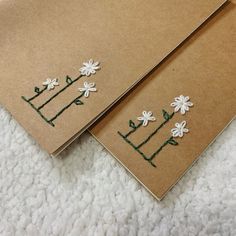 two brown envelopes with white flowers on them sitting on a carpeted floor next to each other