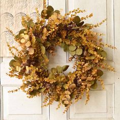 a wreath is hanging on the front door with leaves and other foliages around it