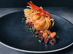 a black plate topped with pasta and shrimp