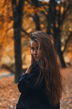 a young woman is talking on her cell phone in the park with leaves all around her