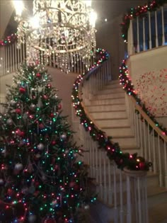 a decorated christmas tree sitting in front of a stair case next to a chandelier