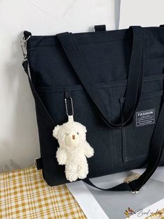 a small white teddy bear hanging from a black tote bag on a yellow and white checkered table cloth