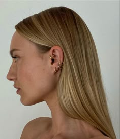 a woman with long blonde hair wearing gold ear climbrs on her left ear, looking off to the side