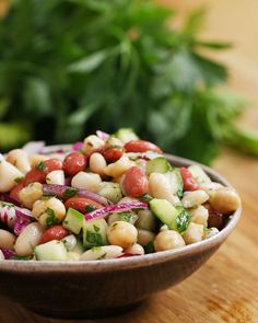 a bowl filled with beans, cucumber and red onion on top of a wooden table