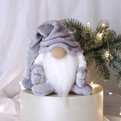 a white and grey gnome figurine sitting on top of a round box next to a christmas tree