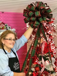 a woman is decorating a christmas tree with red, green and white bows on it