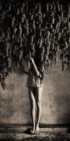 a woman standing in front of a bunch of grapes on a vine covered wall with her hands behind her head