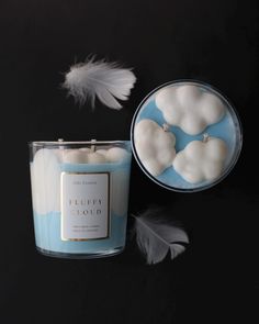 a blue candle with white pumpkins in it next to a feather on a black background