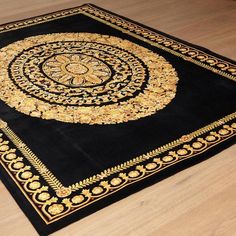 a black and gold rug with an intricate design on the center is sitting on a wooden floor