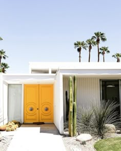 a yellow door sits in front of a white house with cactus and cacti