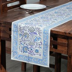 a blue and white table runner on top of a wooden table with a plate in the middle