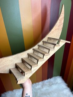 a hand holding a wooden stair case in front of a colorful wall with stripes on it