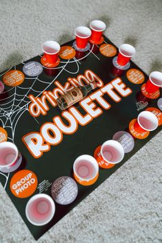 an orange and black board game on the floor with cups around it that says drinking roulette