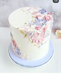 a white cake with pink, purple and blue flowers on the top is sitting on a plate