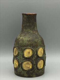 a green and yellow vase with holes in the middle on a gray background, it appears to be made out of clay