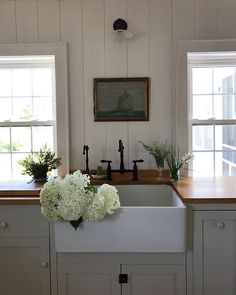 a kitchen with white cabinets and flowers on the counter top in front of two windows