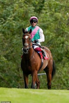 a man riding on the back of a brown horse down a lush green field with trees in the background